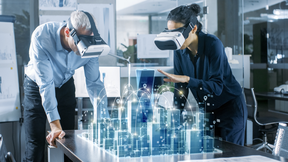 Male and female architects wearing Virtual Reality goggles, examine a 3-D model of a town